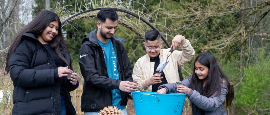 A group of children and a staff member engage in a hands-on planting activity at Darts Hill Garden during a Family Day event.