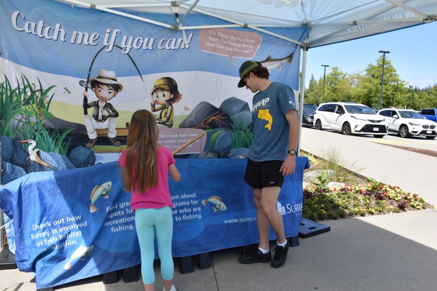 Outdoor booth with an educator engaging a child in a fish habitat awareness activity.