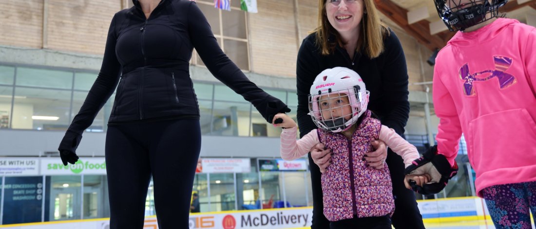 Two adults with two children ice skating.