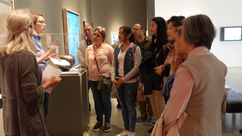 A staff member speaks about artwork in a gallery space to a group of people.